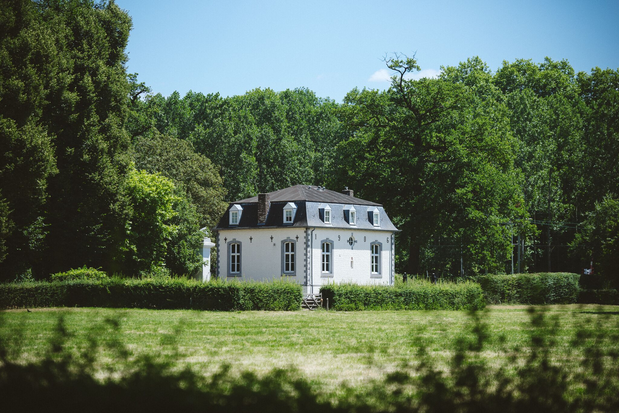 A white house with a dark roof, surrounded by a well-maintained lawn and dense trees.