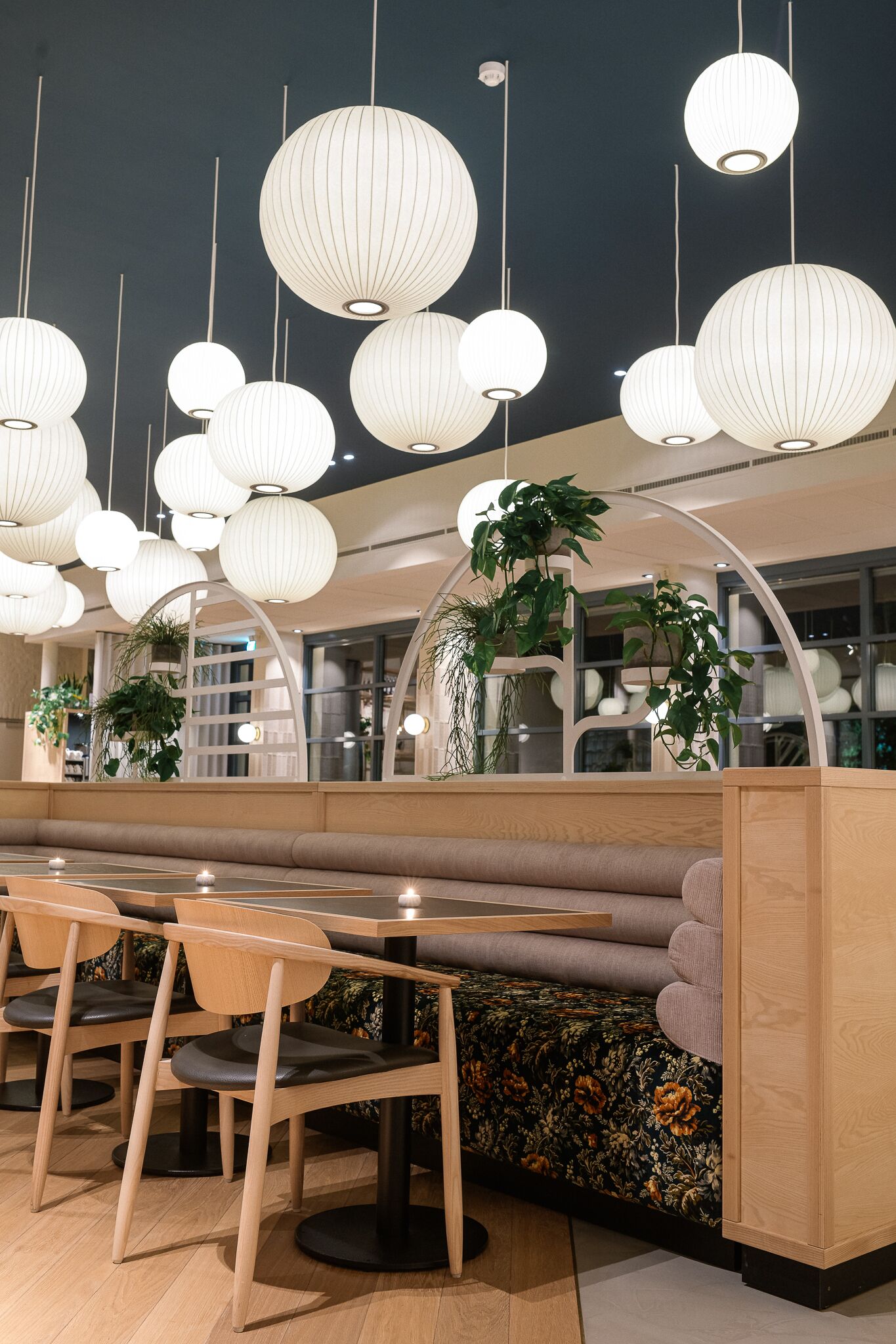 Un intérieur de restaurant moderne, avec des meubles en bois, des lanternes en papier suspendues et des plantes en pot.