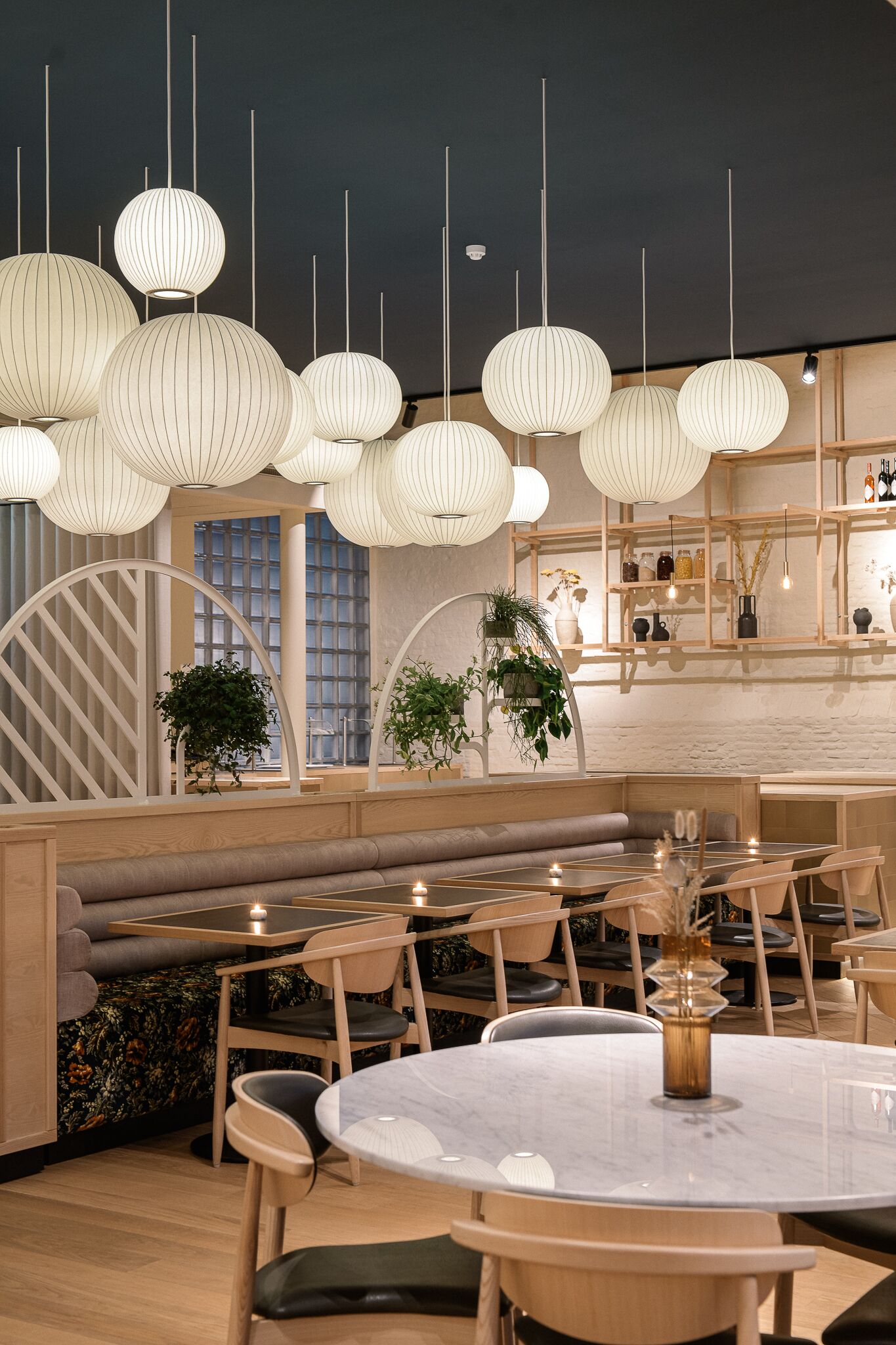 Un intérieur de restaurant moderne avec des tables rondes, des sièges rembourrés, des luminaires suspendus et des éléments décoratifs en bois.