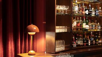 Een bar met een houten toonbank, een lamp en een plank met drankflessen.