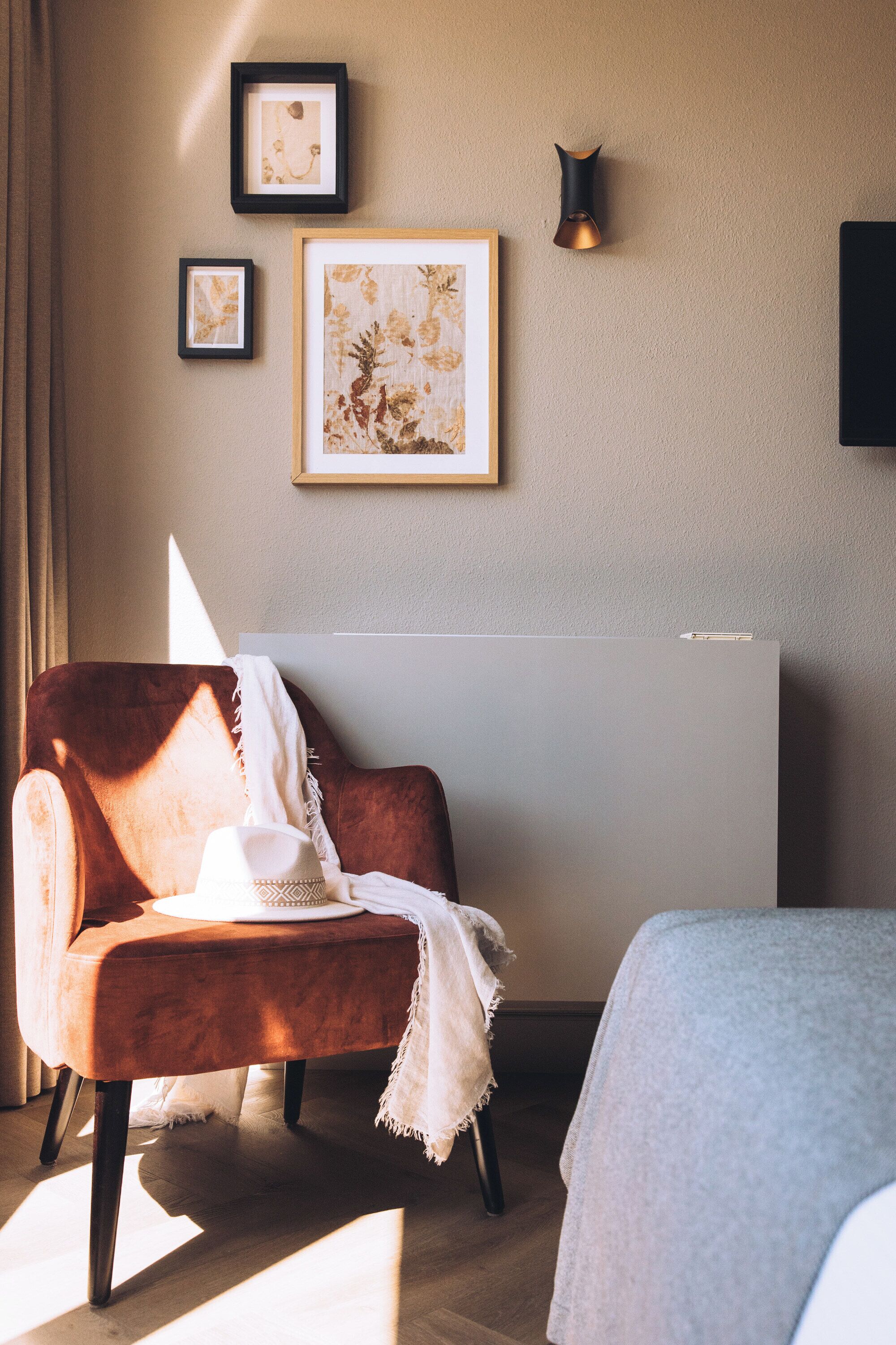A room with a brown chair, a bed, and a wall-mounted light fixture.