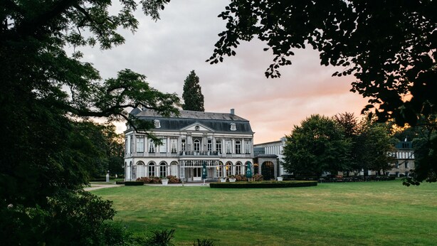 A large, historic building with a symmetrical facade, a central entrance, and a well-maintained lawn in front.