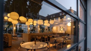 A restaurant with round tables and chairs, hanging paper lanterns, and a view of the street through large windows.