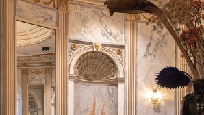 A luxurious interior with marble walls, a large mirror, and elegant furnishings including a sofa and round tables.