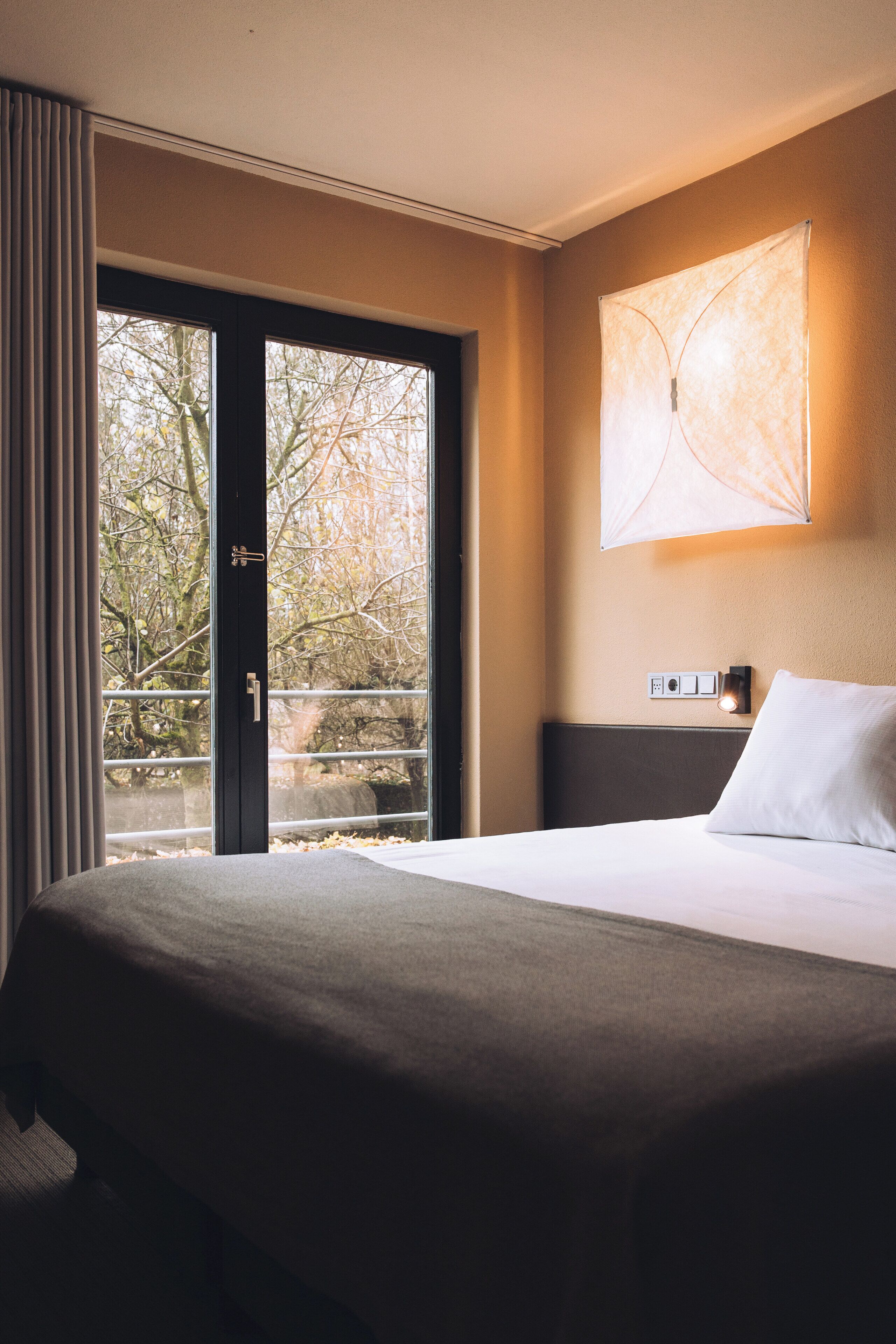 Una habitación de hotel con una cama grande, una puerta corrediza de vidrio a un balcón y una lámpara fijada a la pared.