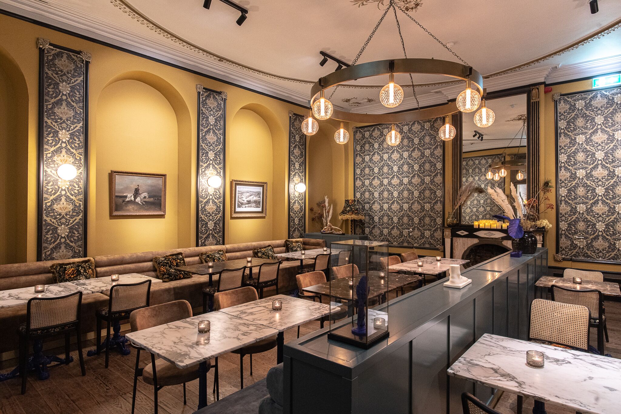Un restaurant doté de tables et de bancs aux plateaux en marbre, de décorations murales élaborées et d’un bar central.