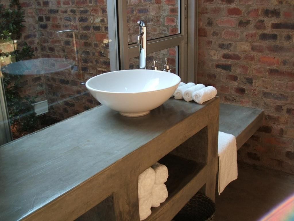 A bathroom with a large white vessel sink, a wooden vanity, and a brick wall.