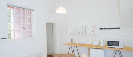 A bright, spacious room with a wooden dining table, yellow chairs, a white ceiling, and a kitchen area with a microwave.