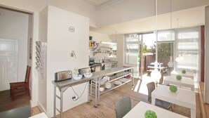 A modern kitchen with stainless steel appliances, a dining area with white tables and chairs, and a large window providing natural light. - motel Mi Pi CHi (Johannesburg)