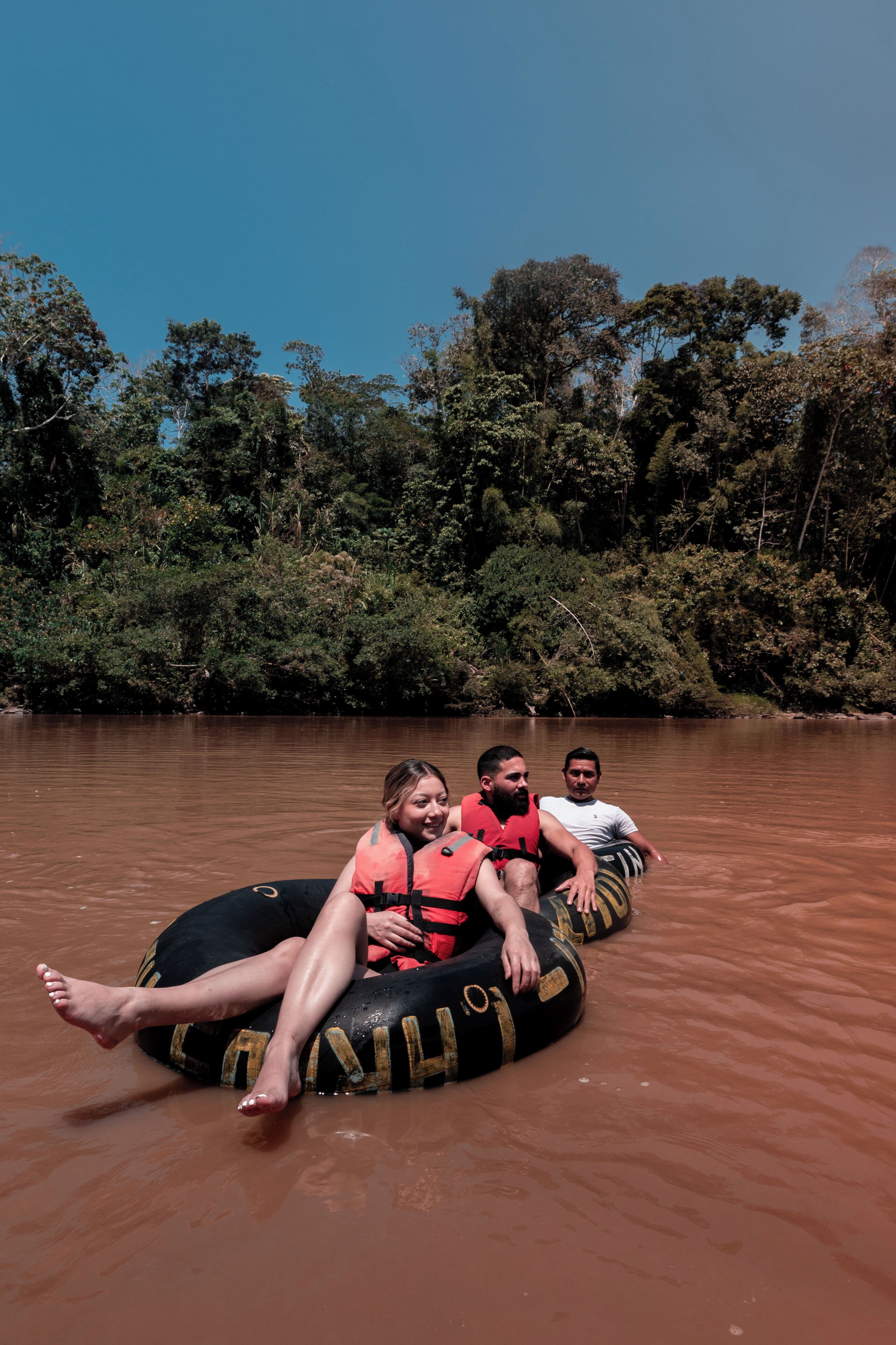 Tres personas en un bote en un río rodeado de árboles.