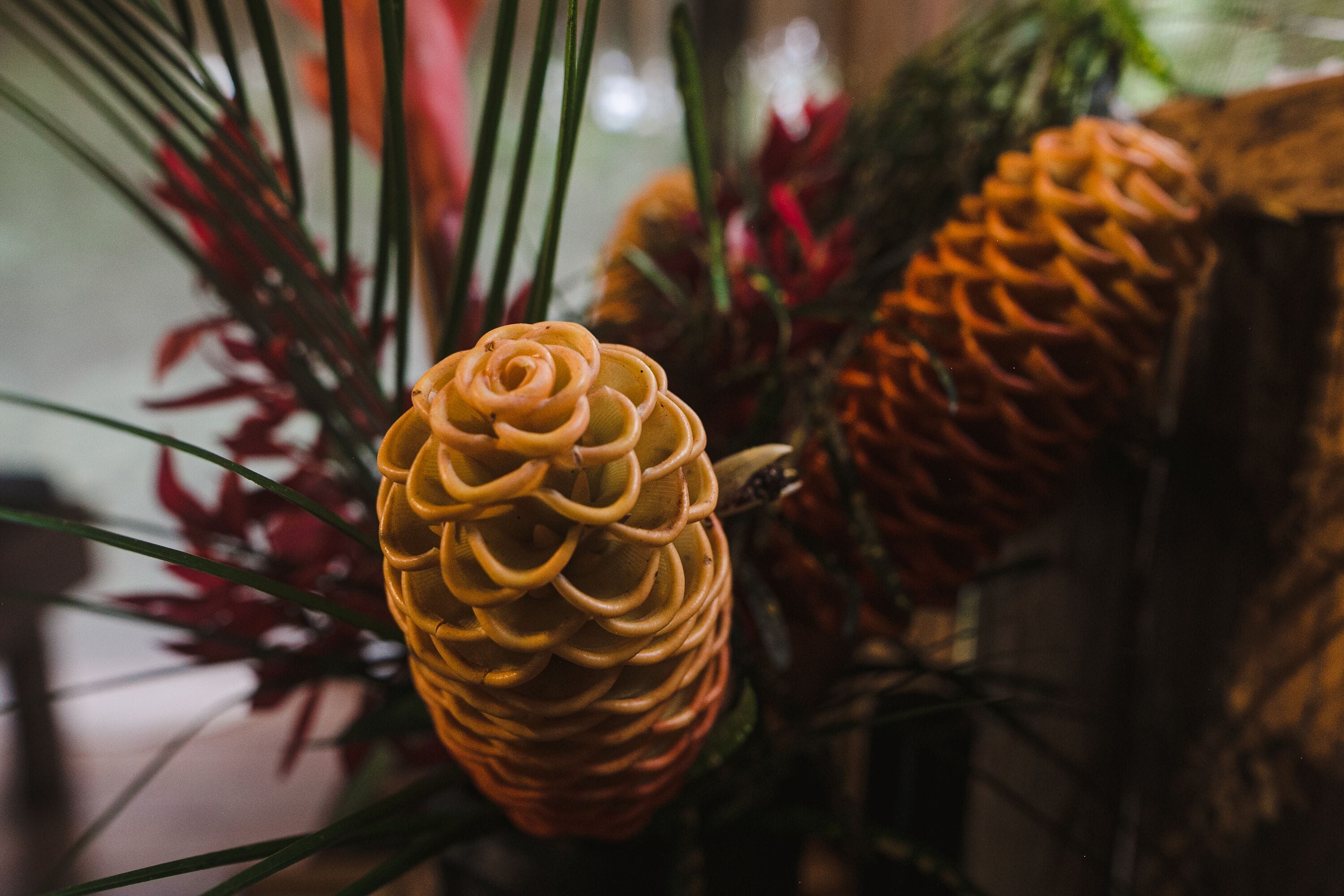 A close-up of a pineapple with a spiral pattern, surrounded by green leaves and red flowers.
