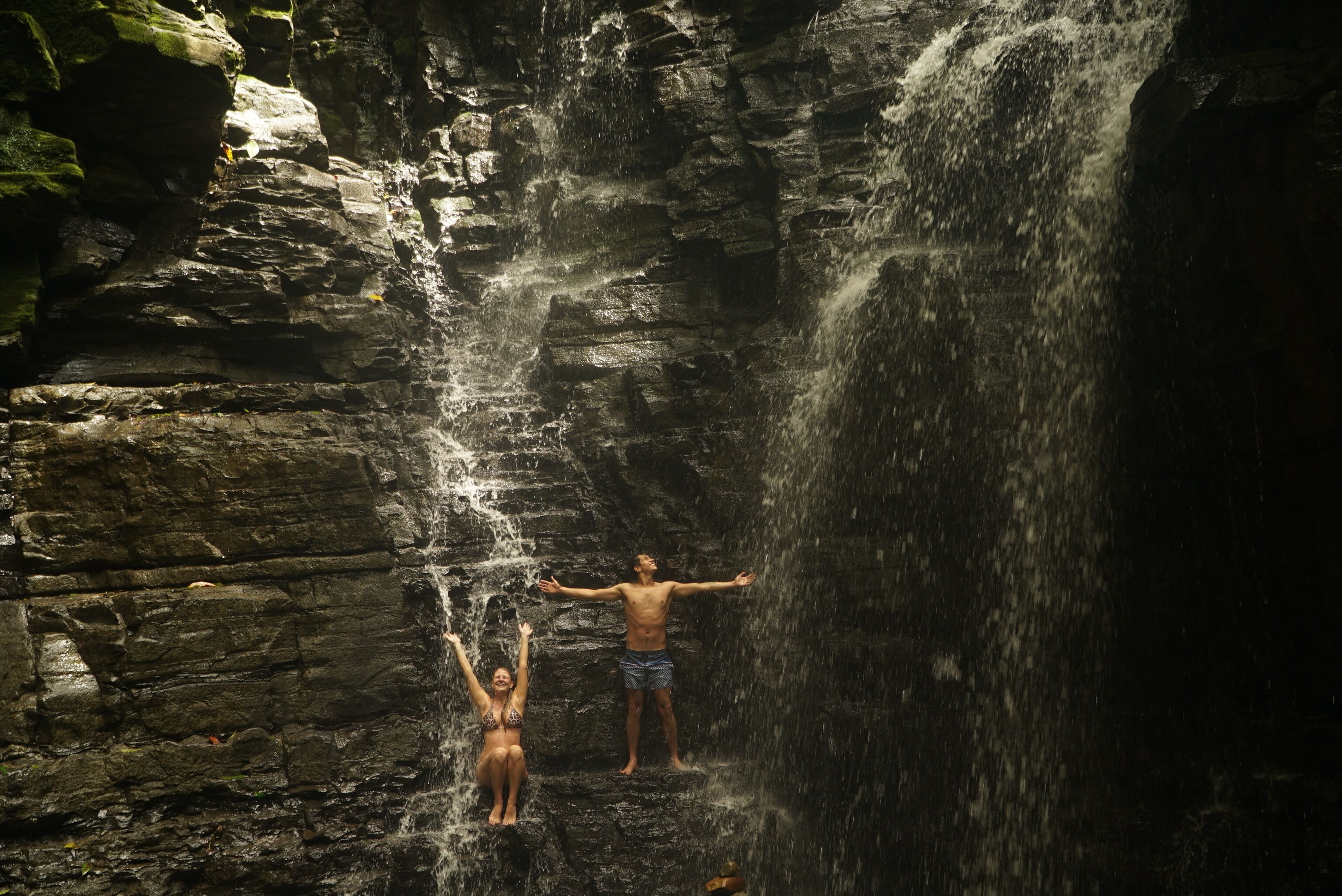 Una cascada en un entorno rocoso con dos personas admirando la vista.