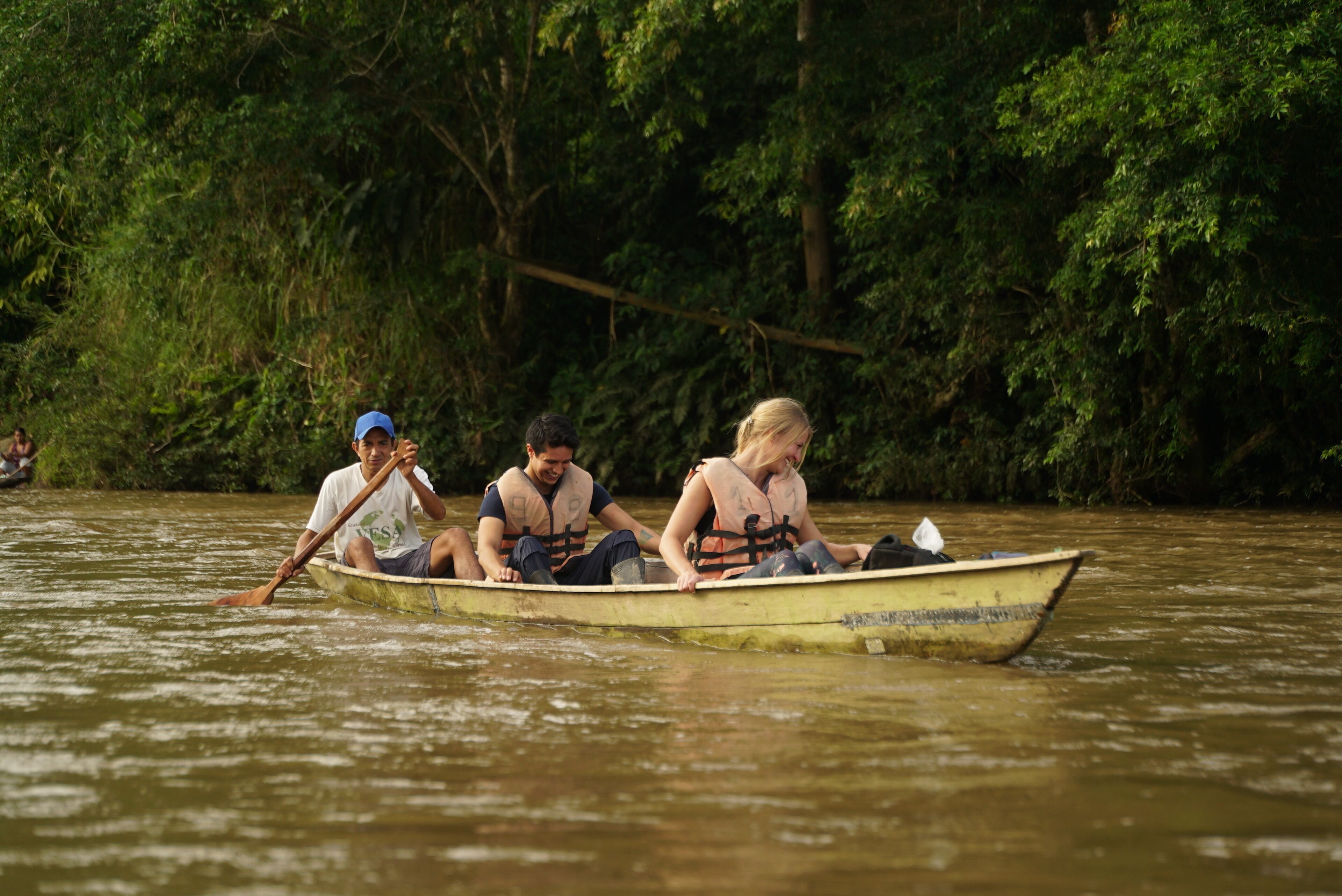 A group of people in a small boat on a river surrounded by dense greenery.