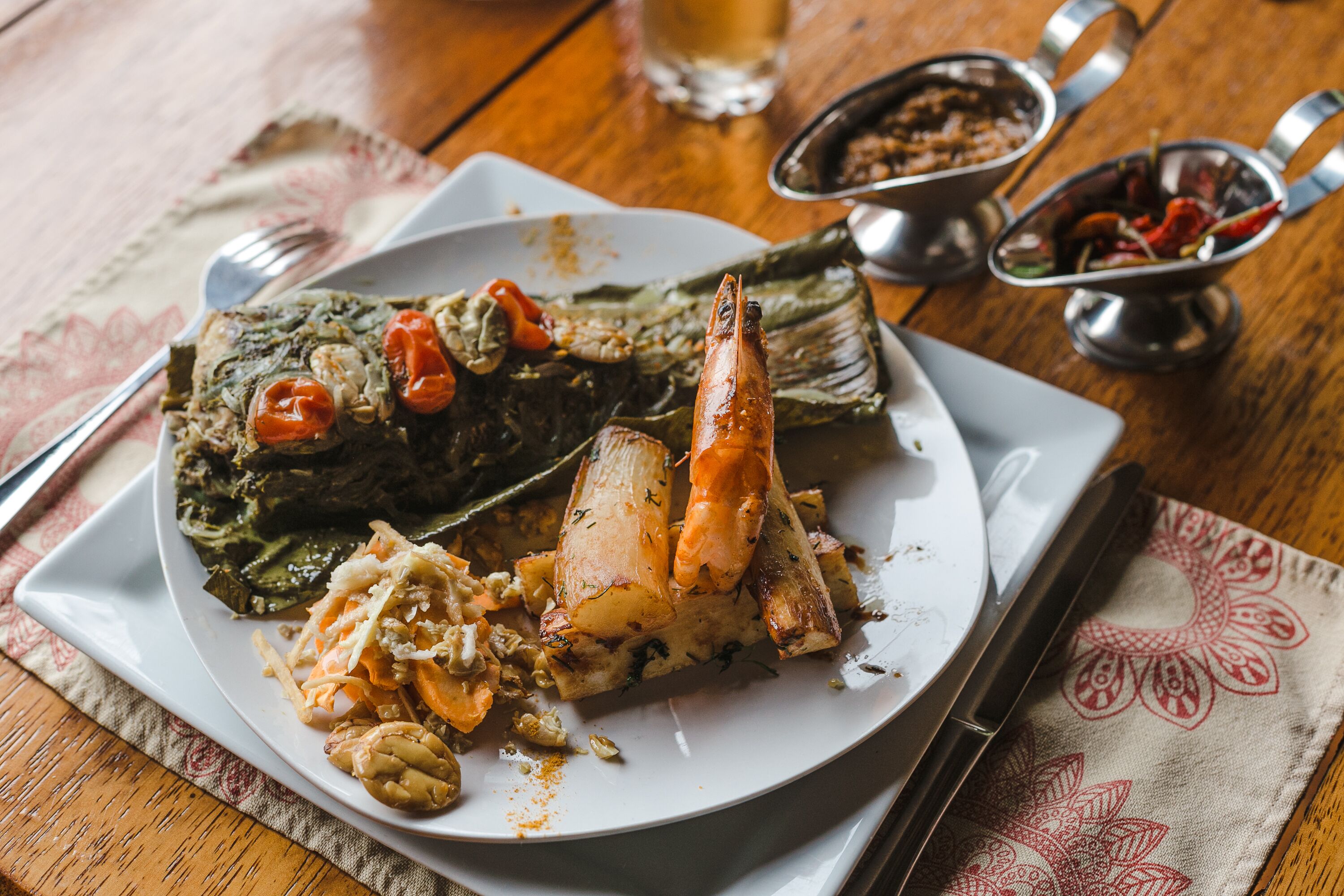 Un plato de comida con pescado, verduras y salsa sobre una mesa de madera.