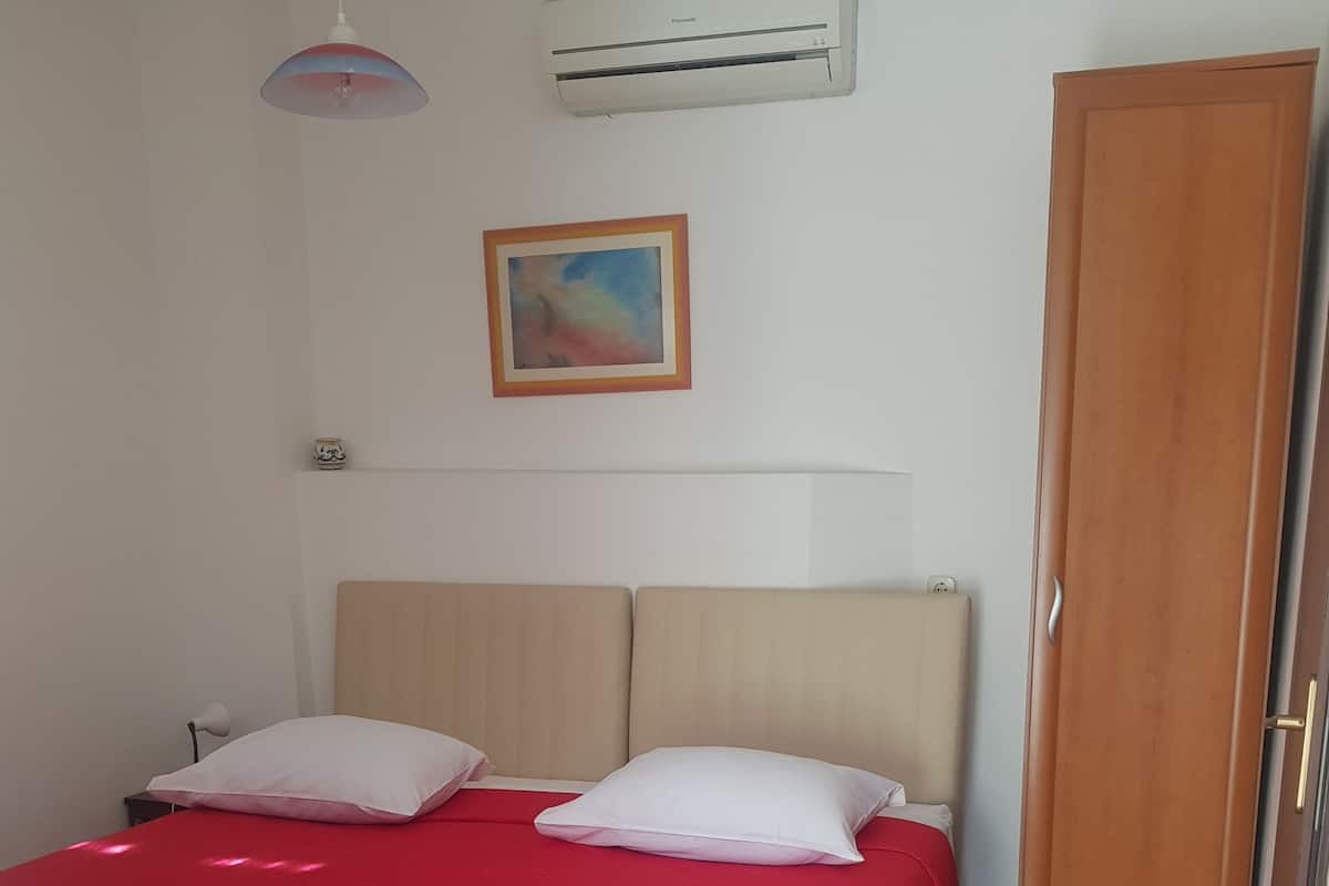 A bedroom with a bed, a wardrobe, a wall-mounted air conditioner, a ceiling light, and a framed picture.