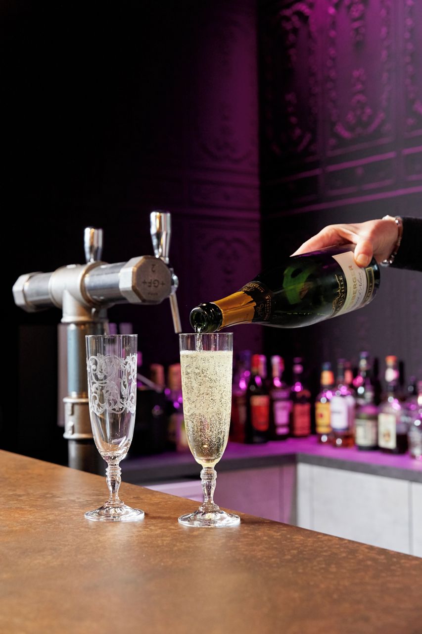 A bar setting with a hand pouring champagne into a glass.