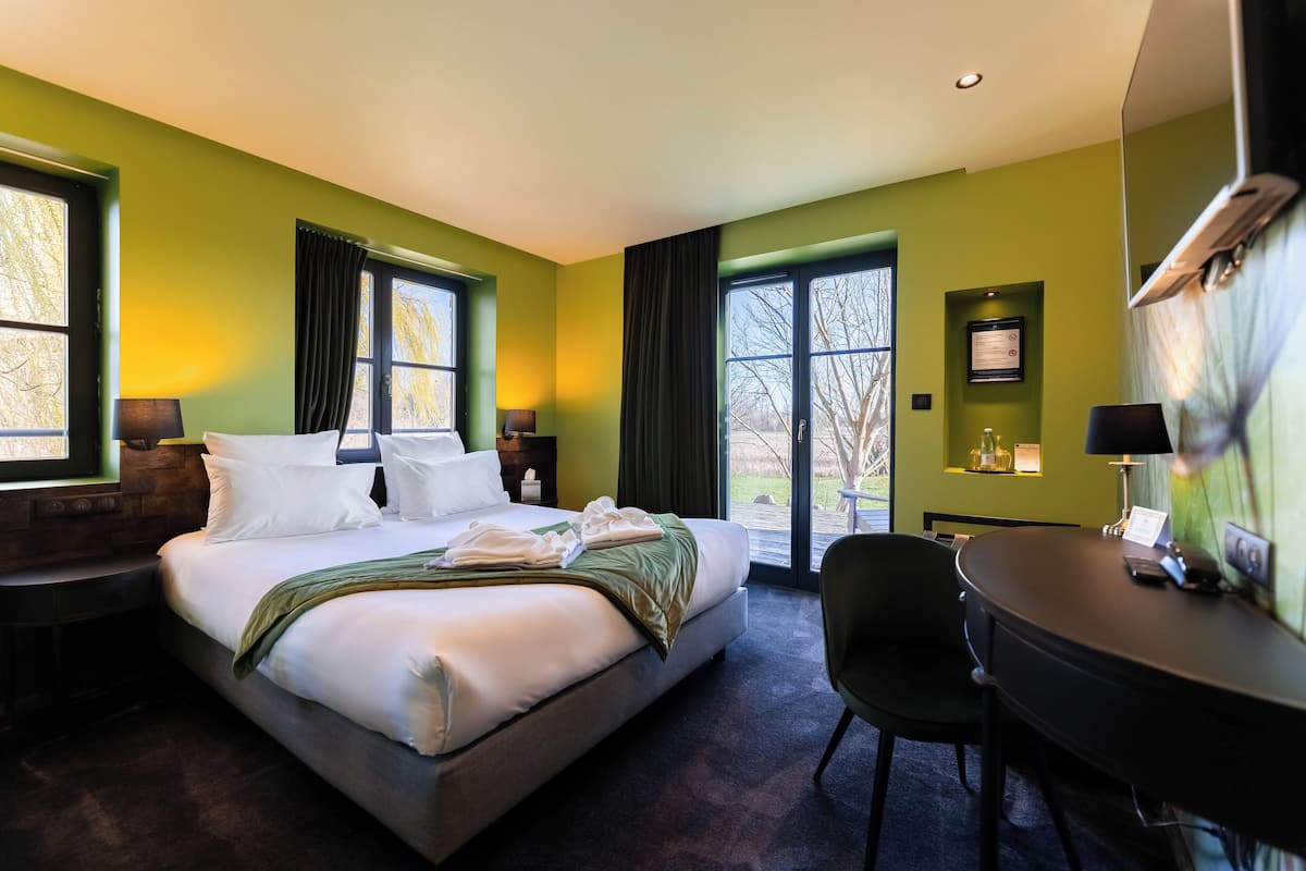 Une chambre d’hôtel avec un grand lit, un bureau et une chaise. Elle est équipée de deux fenêtres avec des rideaux, d’un climatiseur fixé au mur et d’un certificat encadré accroché au mur.