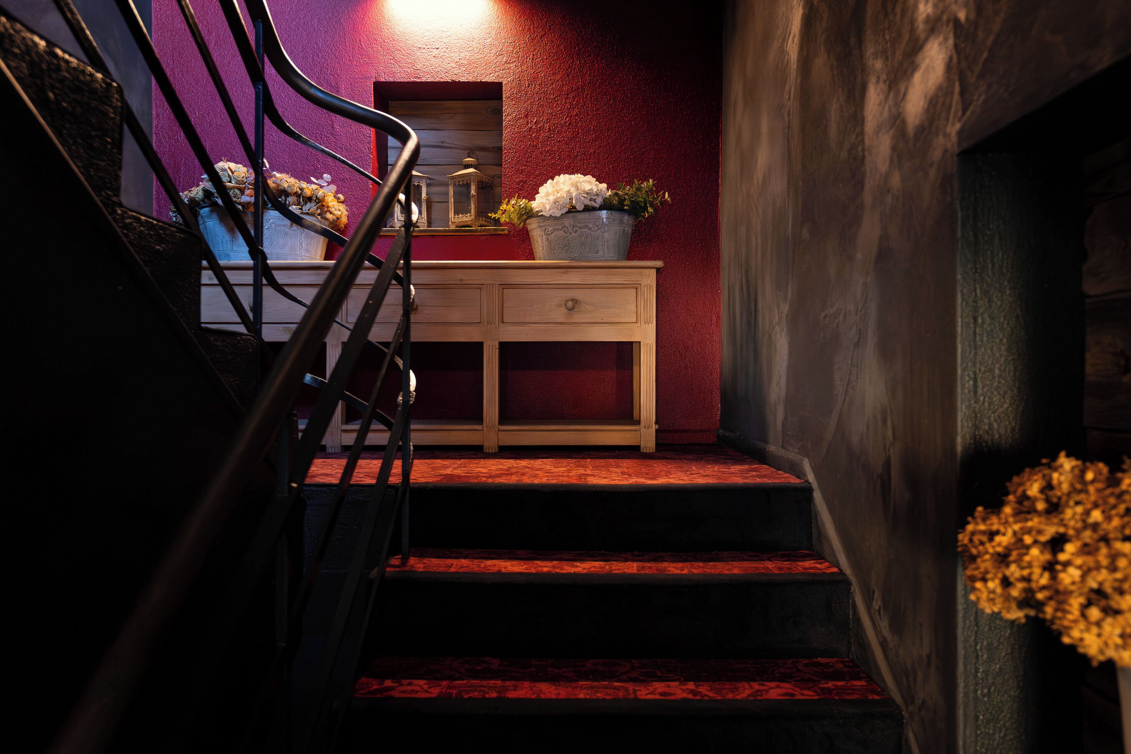 Un escalier recouvert d’une moquette rouge, une console en bois ornée d’une plante en pot et une rampe en métal.