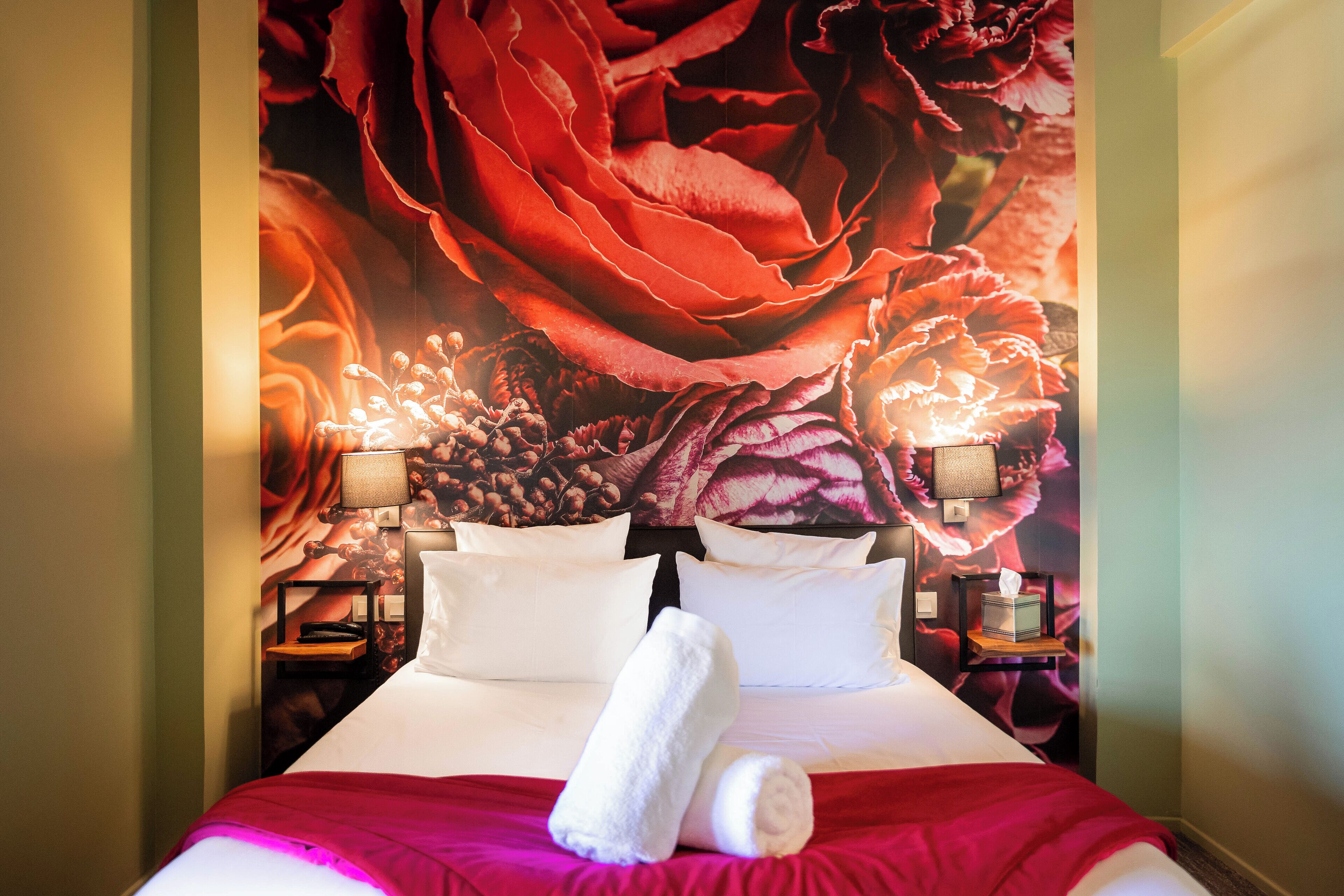 Ein Hotelzimmer mit einer großen floralen Wandmalerei, einem ordentlich bezogenen Bett mit weißer Bettwäsche und zwei Nachttischen mit Lampen.