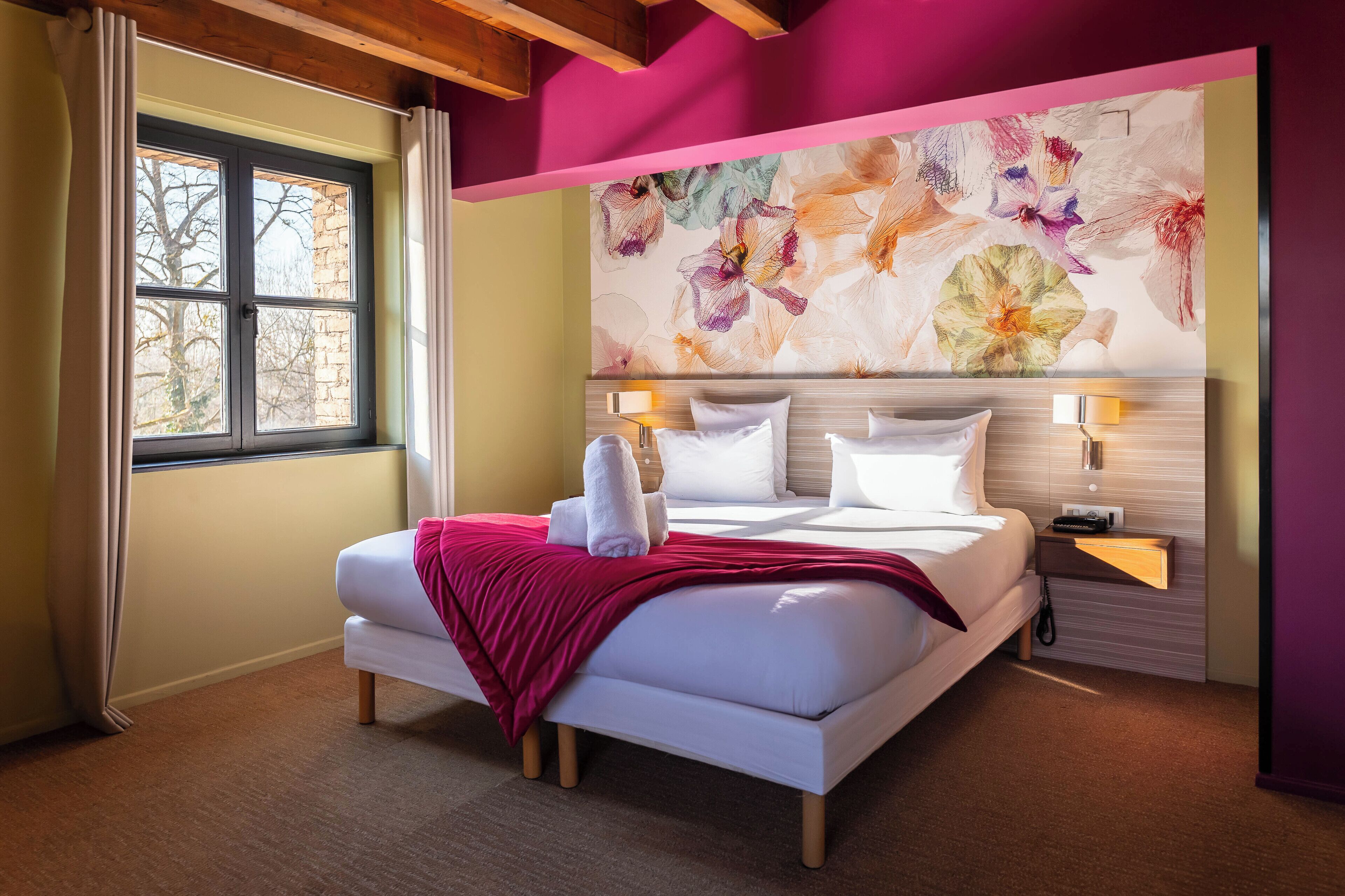A hotel room with a large bed, a window with curtains, a wall-mounted artwork, and bedside lamps.