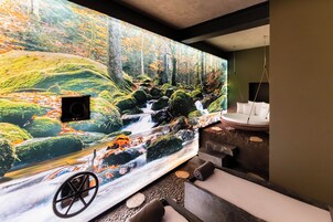Un espace de bien-être comprenant une fresque représentant un ruisseau de forêt, un fauteuil de massage et une baignoire.
