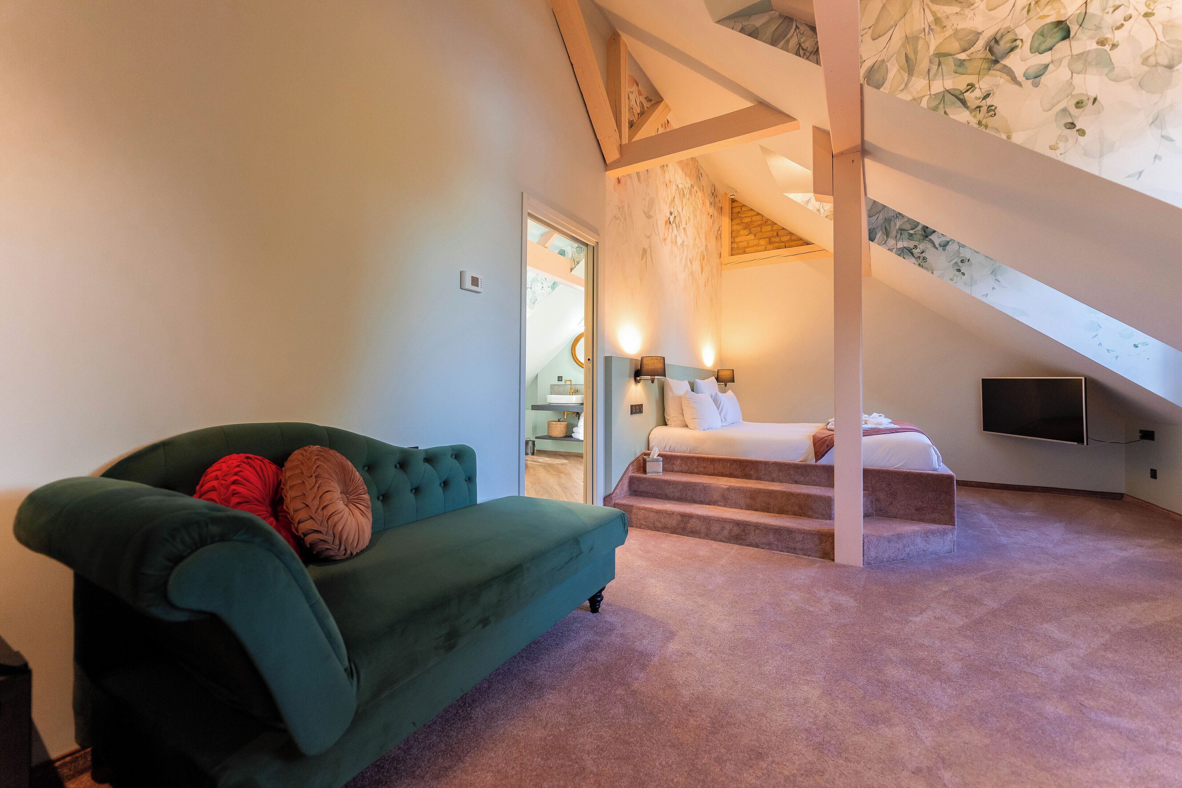 Ein Zimmer mit einem grünen Sofa, einem Bett, einem Fernseher und einer Treppe zu einer oberen Ebene.