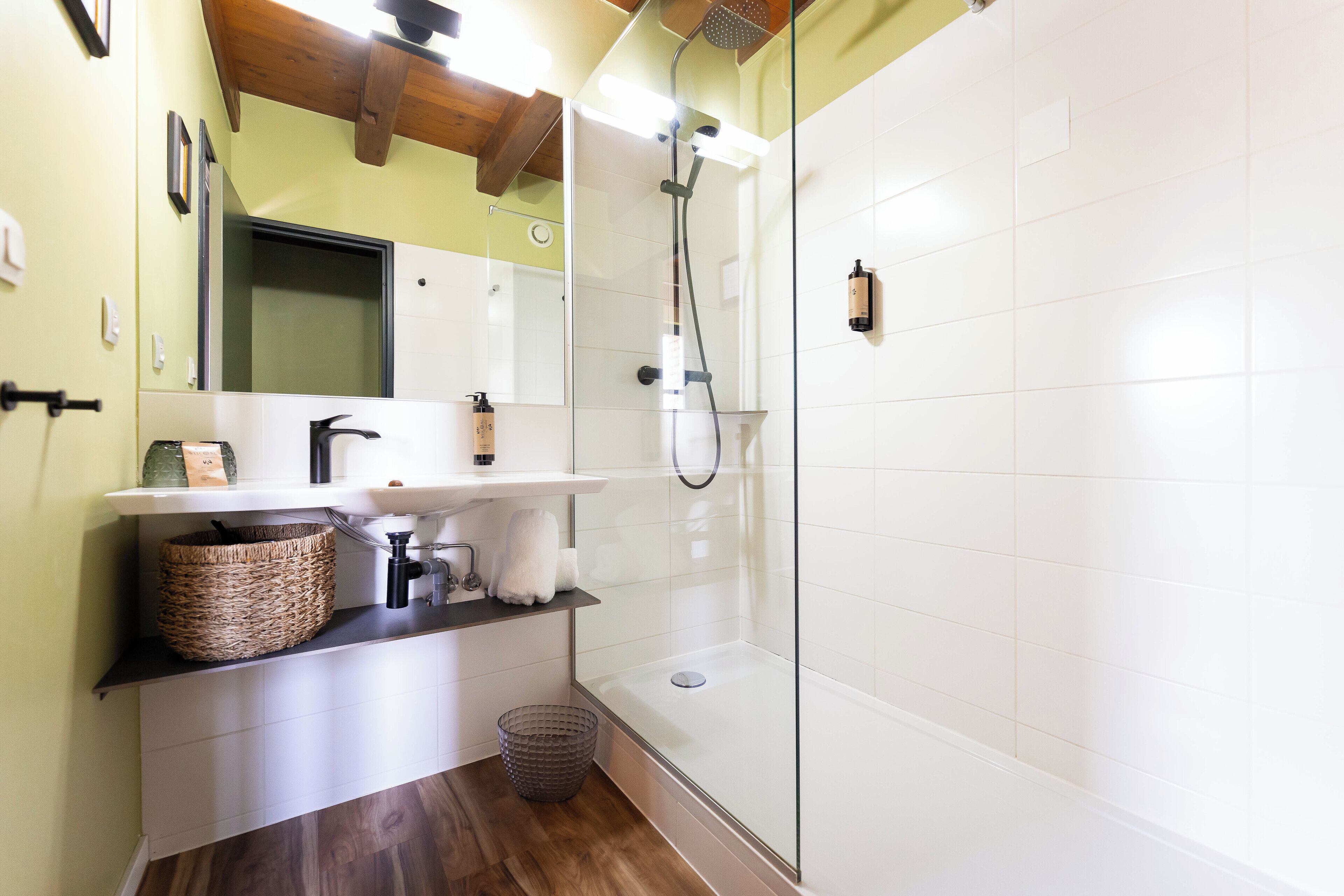 A modern bathroom with a glass-enclosed shower, a white sink, and a wooden floor.