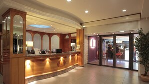 A hotel reception area with a wooden reception desk, a large mirror, and a glass door leading to the bar area. - Pascal Paoli (Aregno)