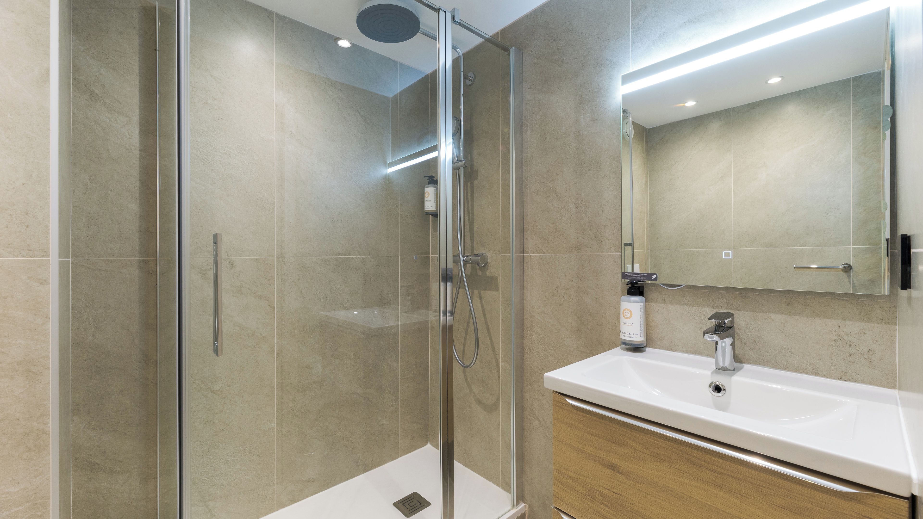Een moderne badkamer met een douche in een glazen cabine, een wit wastafeltje en een grote spiegel.
