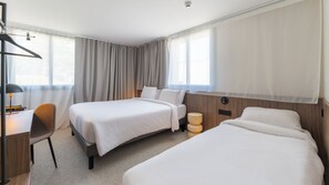 Une chambre d’hôtel avec deux lits, un bureau avec une chaise et une lampe.