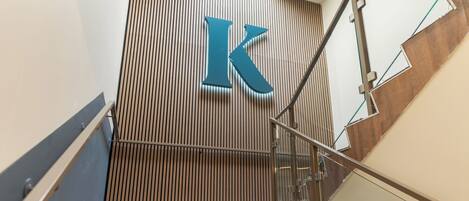 A modern building with a prominent 'K' sign on a wooden panel wall, a glass railing, and a metal staircase.