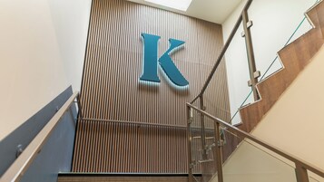 Un edificio moderno con un llamativo letrero 'K' en un panel de pared de madera, barandilla de vidrio y escalera de metal.