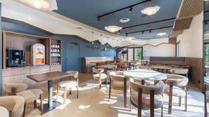 Un intérieur de restaurant moderne offrant différents types de sièges, notamment des tables et des banquettes, ainsi qu’une machine à café sur le comptoir.
