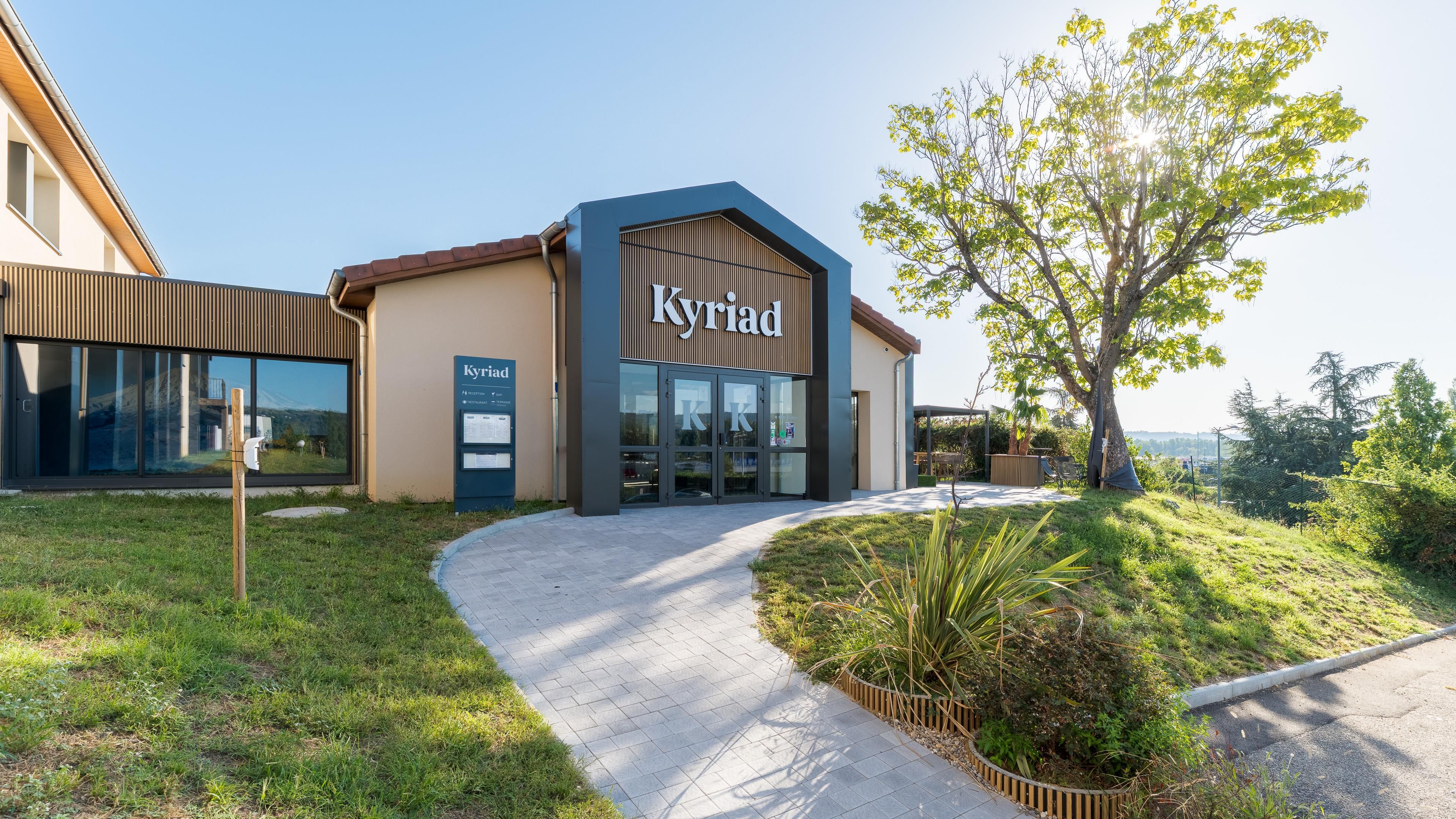 A modern building with a sign reading 'Kyriad' and a reception desk.