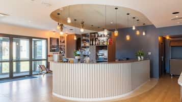 A modern bar area with a curved counter, hanging pendant lights, and a variety of bottles and glasses.