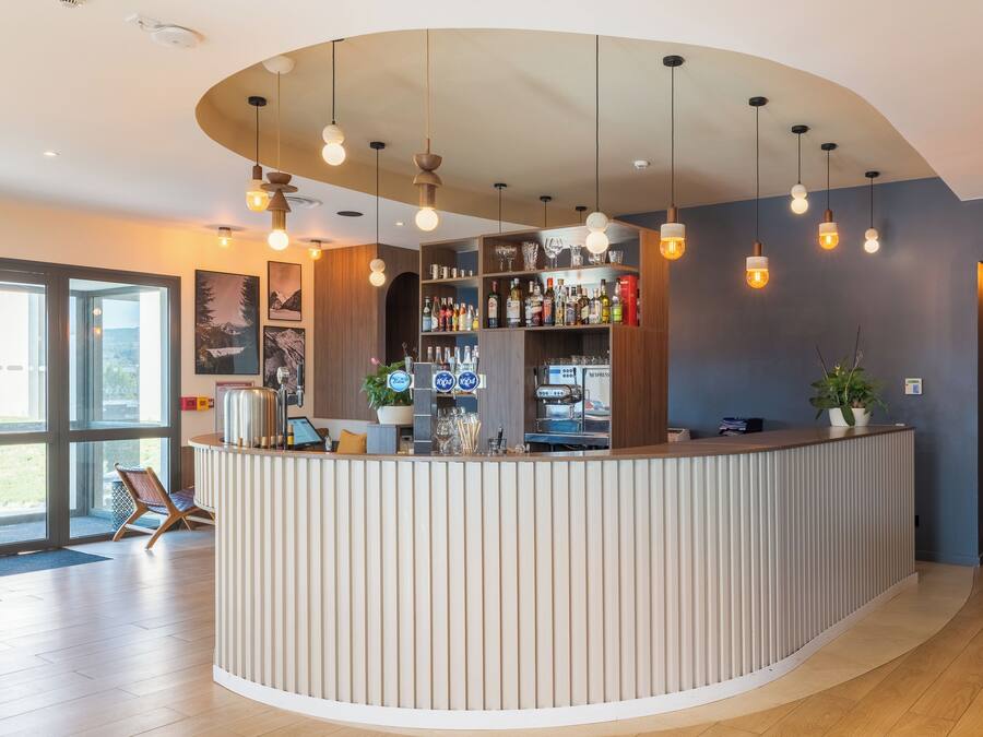 Zona de bar moderna con barra curva, iluminación colgante y vistas al exterior a través de amplios ventanales.