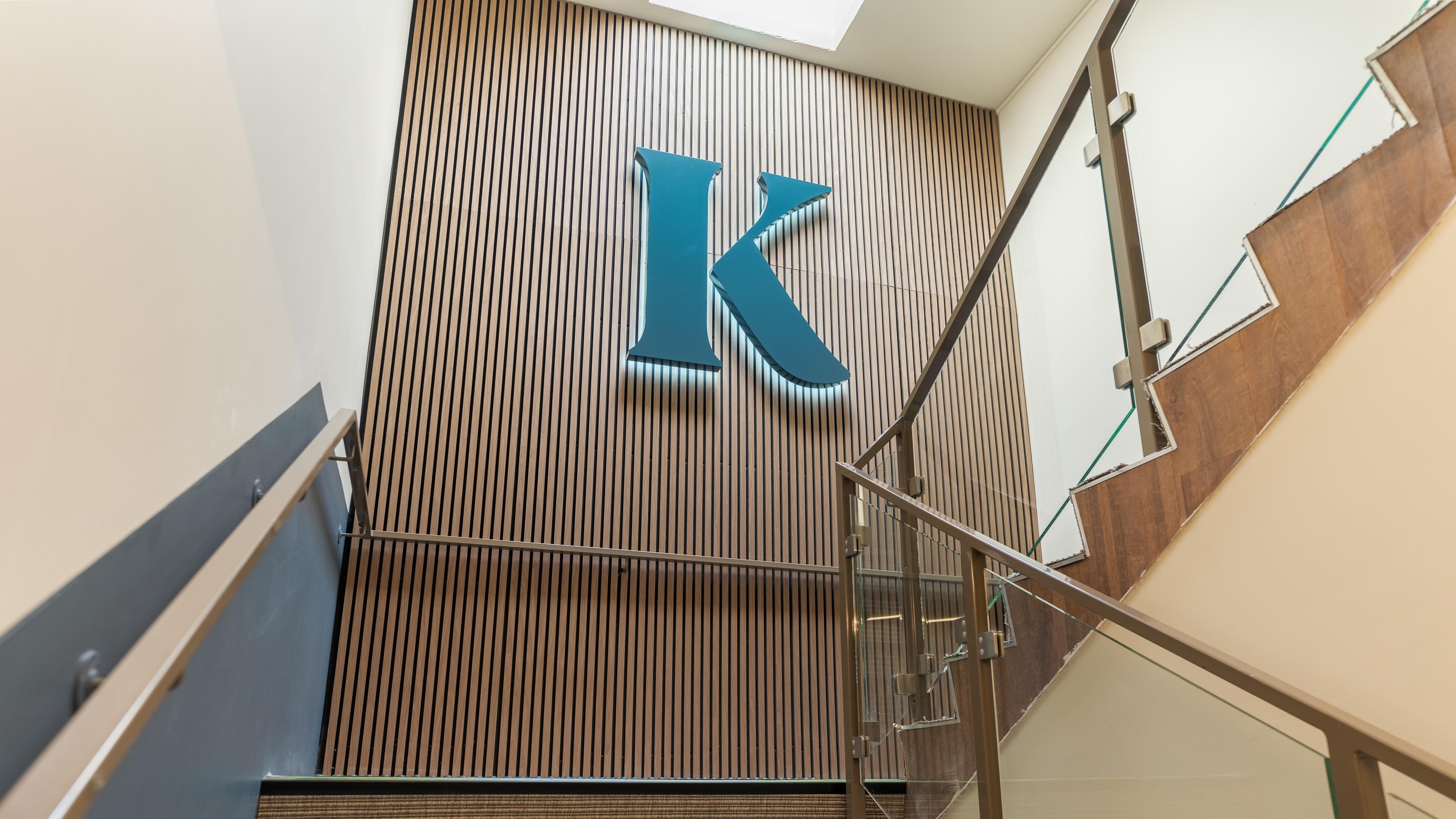 A modern staircase with a wooden panel wall and a large 'K' sign.