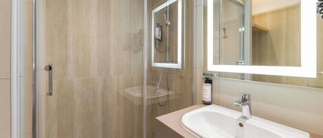 Une salle de bain moderne avec une douche à parois de verre, un lavabo avec un miroir et une douchette à main.