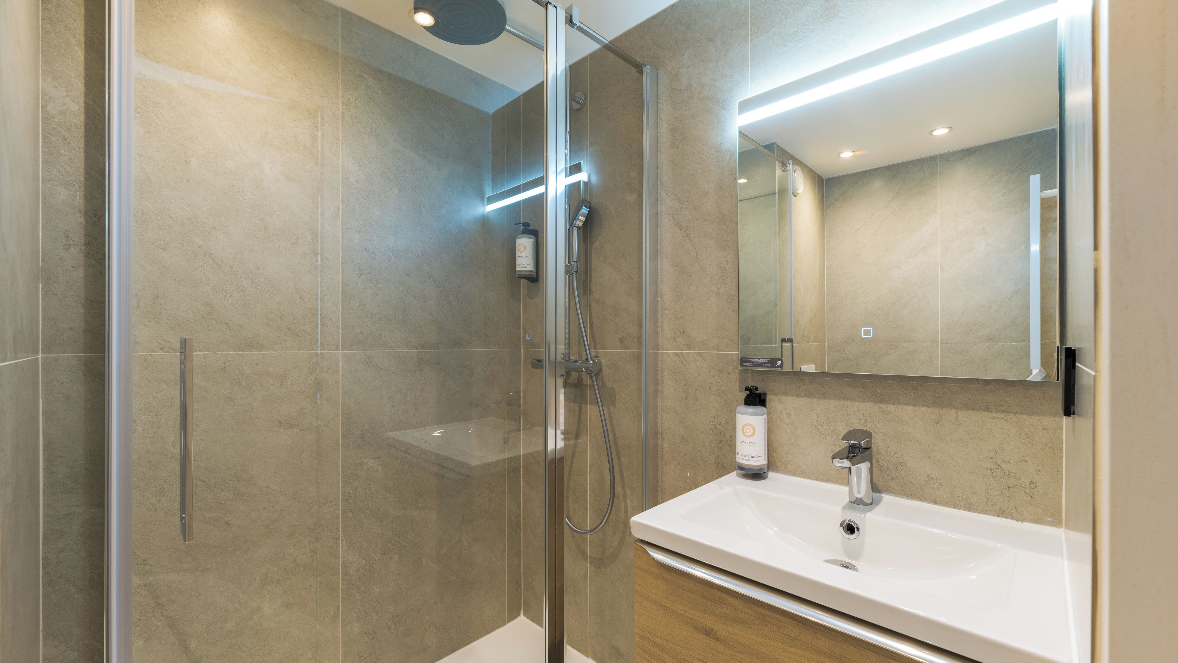 Un baño moderno con ducha de vidrio, un lavamanos blanco y un espejo grande.