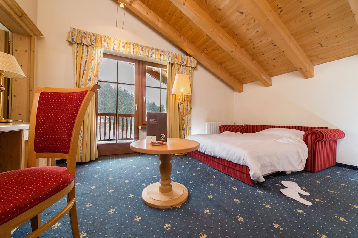 A room with a bed, a chair, a table, and a window with curtains.