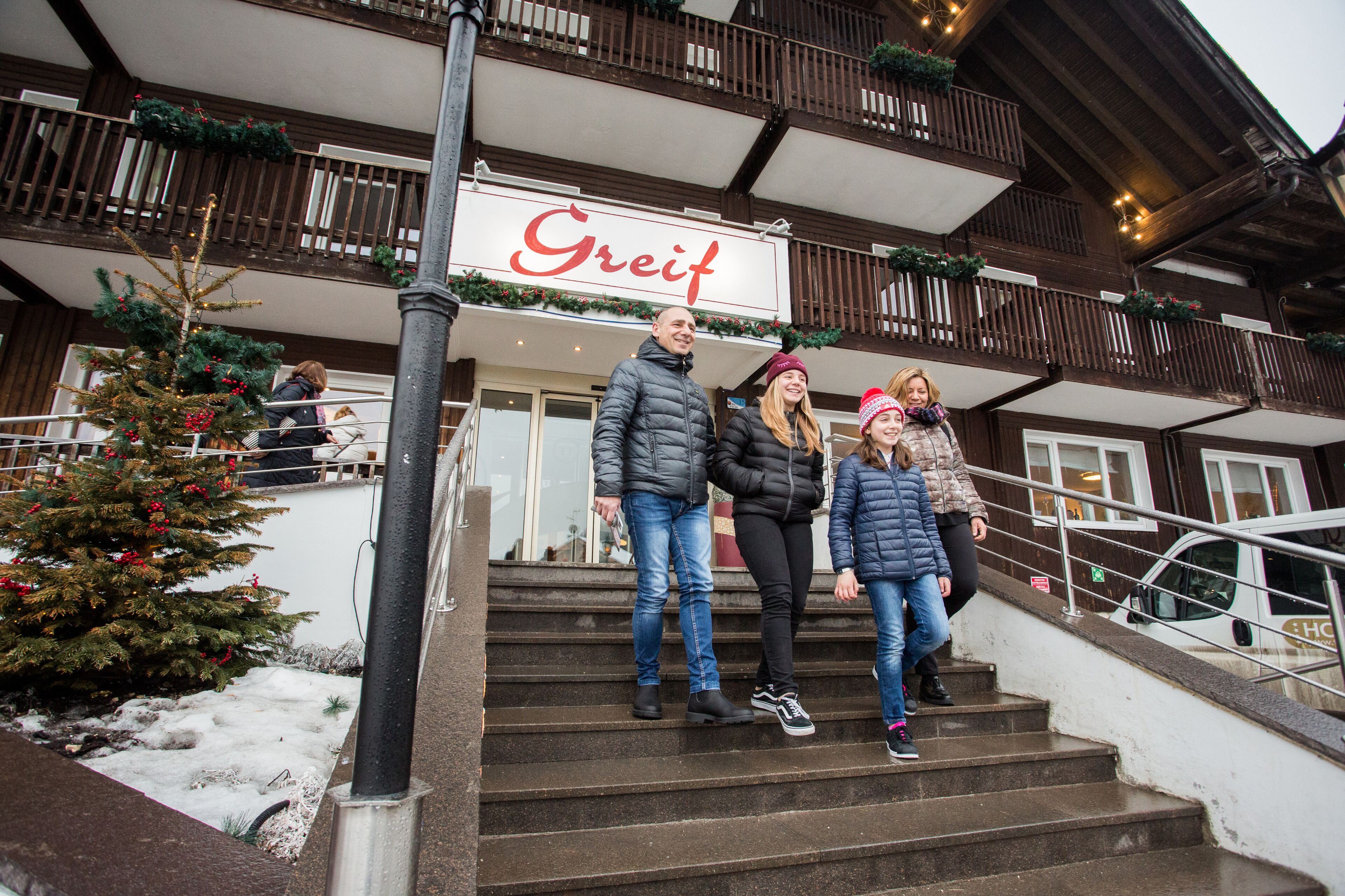 L’entrée d’un hôtel, avec une enseigne portant le nom « Greif », un escalier et un sapin de Noël.