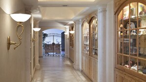 A corridor with tiled flooring, wooden cabinets, and wall-mounted light fixtures. - TH Corvara - Greif Hotel (Corvara in Badia)
