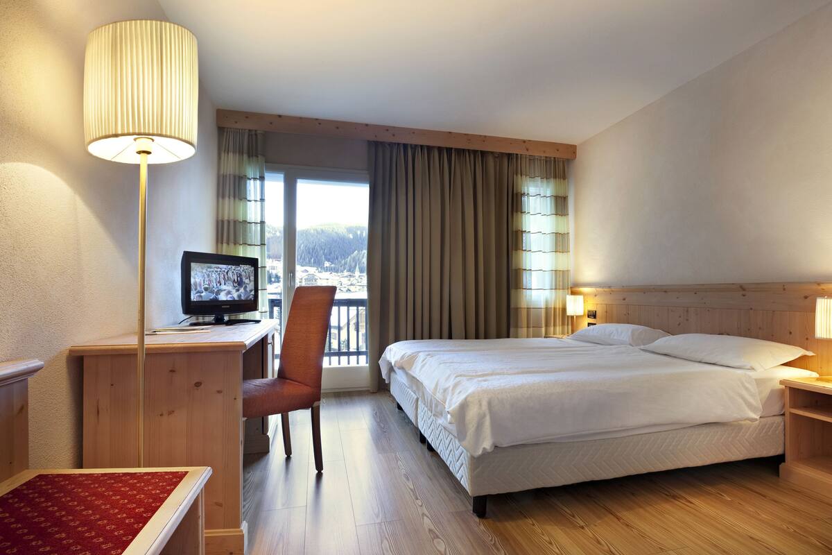 A hotel room with a bed, desk, chair, TV, and a view of the outdoors.