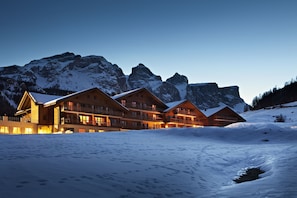 Un'ampia struttura ricettiva con diversi edifici in legno, circondata da montagne innevate e un cielo sereno.