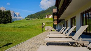A row of sun loungers on a paved patio with a mountain view in the background. - TH Corvara - Greif Hotel (Corvara in Badia)
