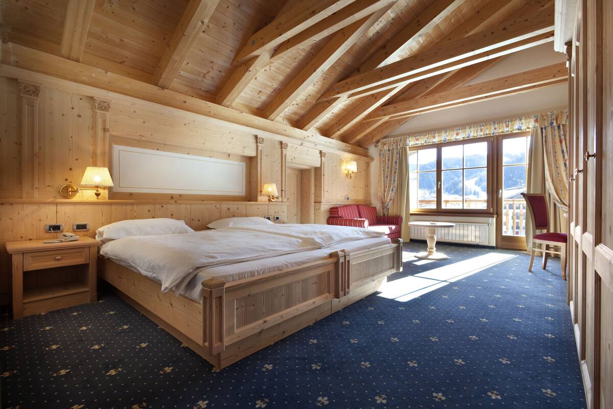 A wooden bedroom with a large bed, bedside tables, a small table, and a chair.