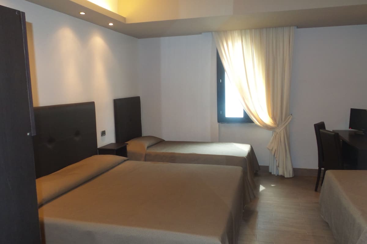 A hotel room with two single beds, a desk with a chair, a TV, and a window with curtains.
