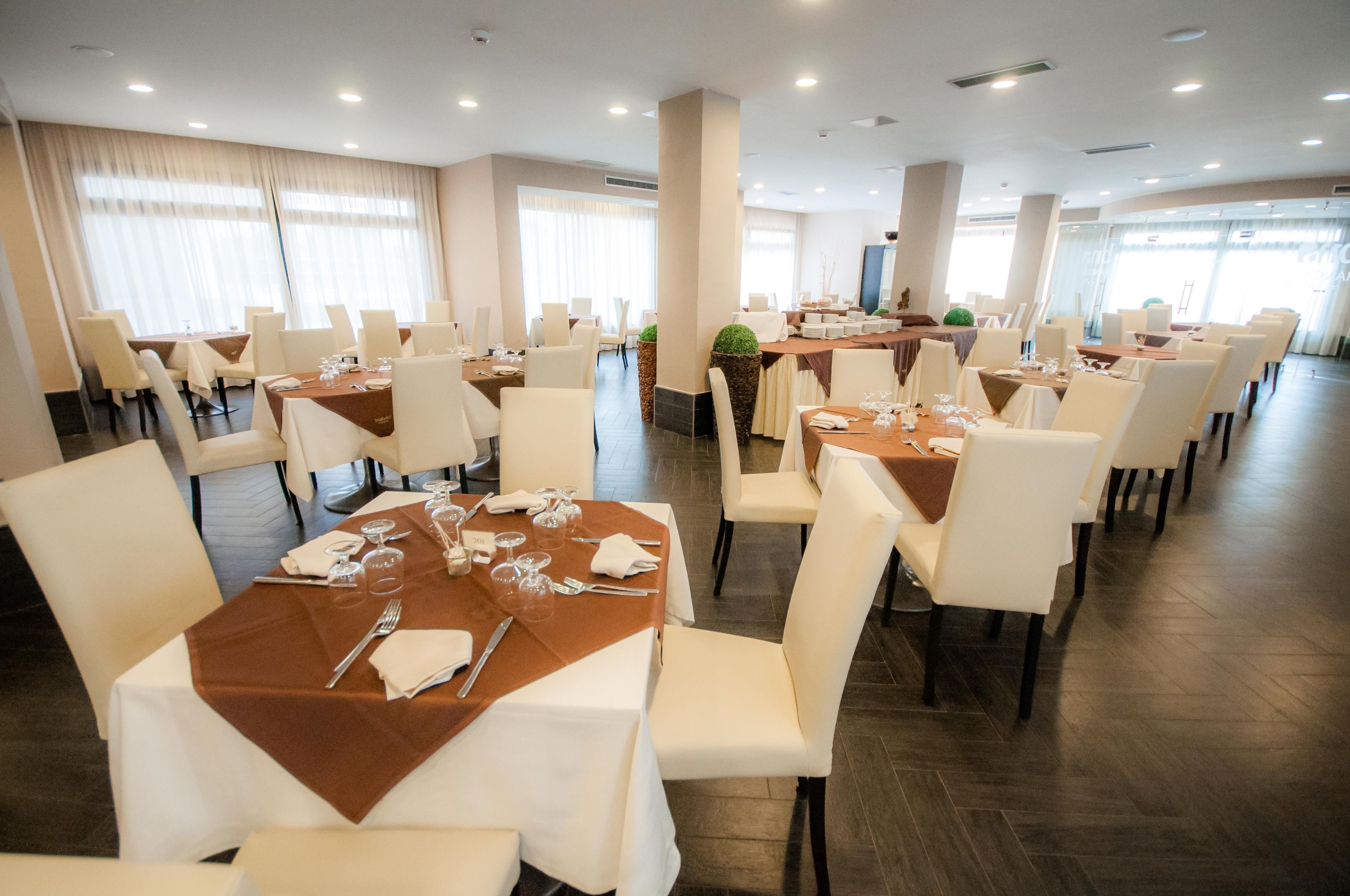 A spacious dining area with multiple tables set for dining, featuring white chairs and brown tablecloths.