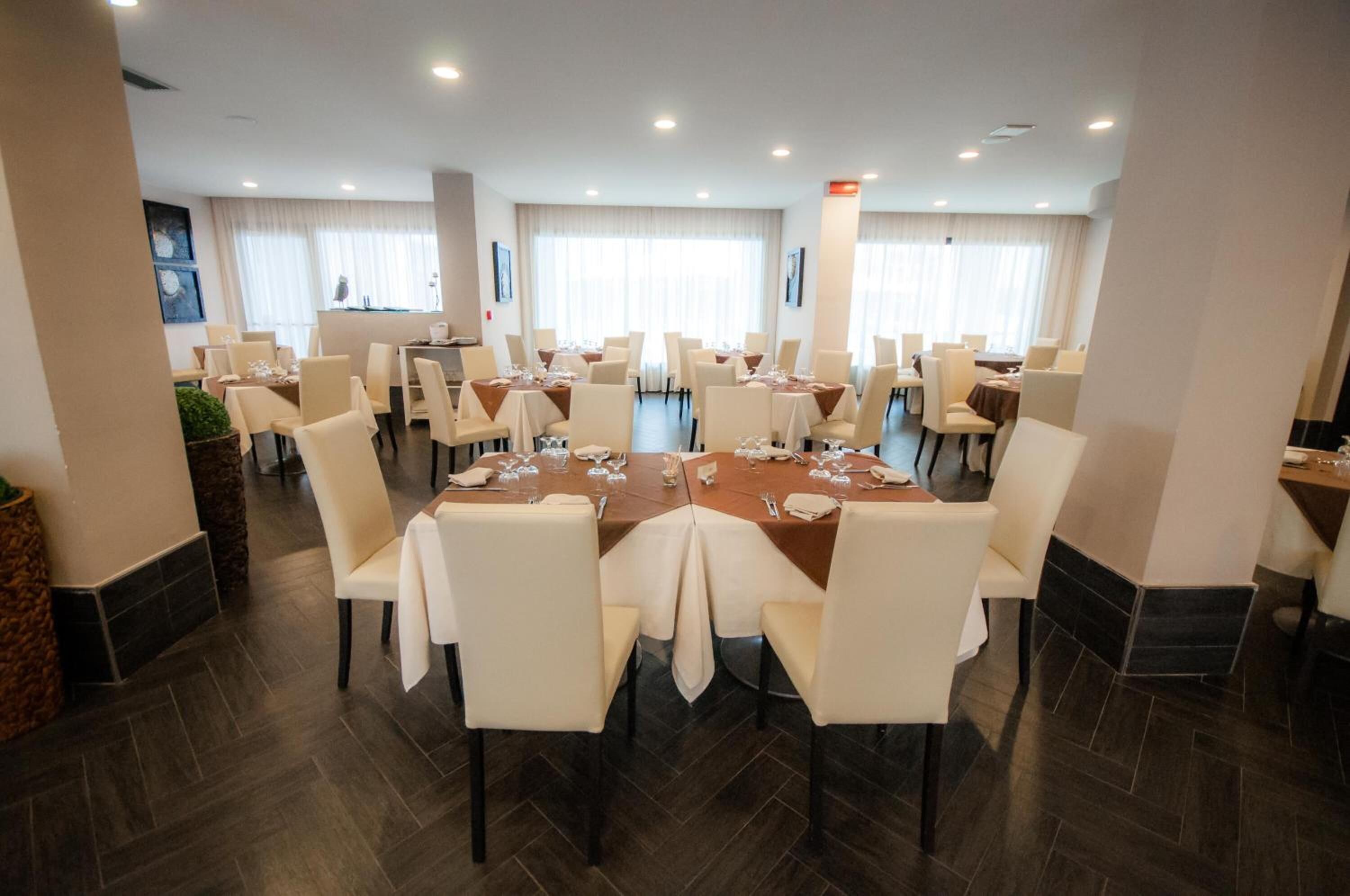 A spacious dining area with multiple round tables and white chairs, arranged in a U-shape.