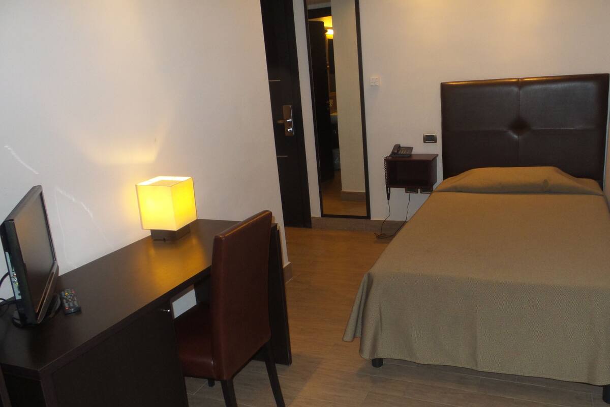 A hotel room with a bed, a desk with a lamp, a chair, and a telephone.